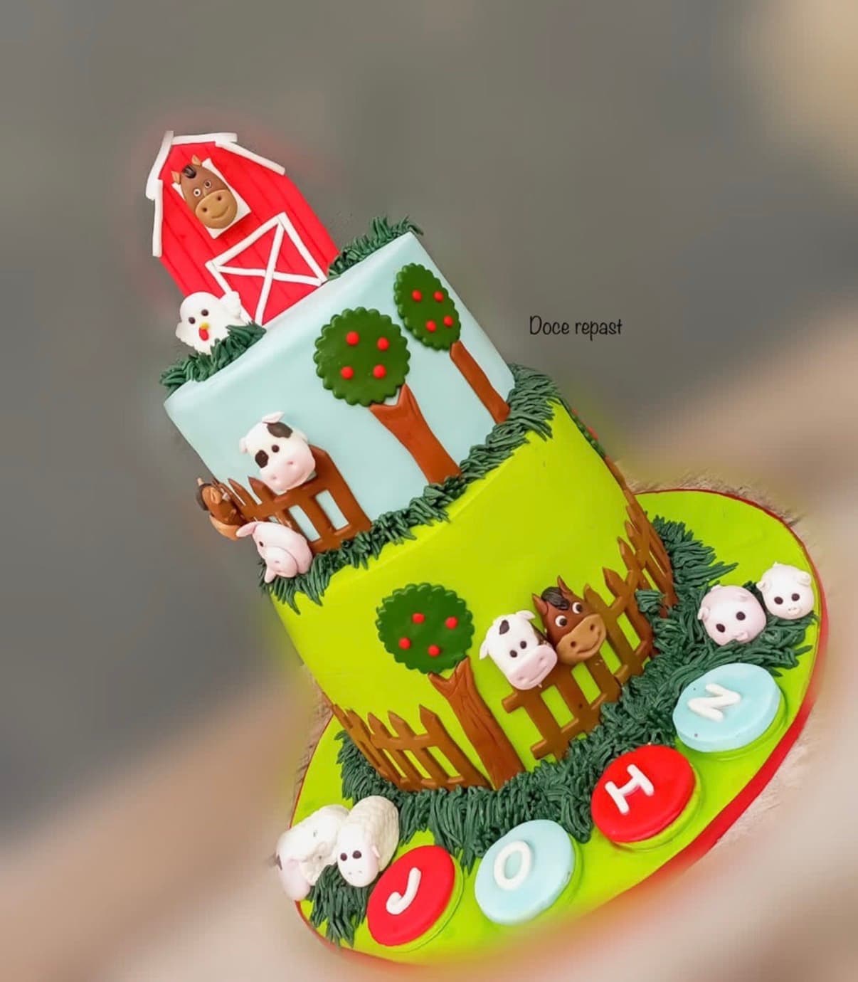 Colorful two-tier farm-themed birthday cake with a barn, animals, trees, and fencing